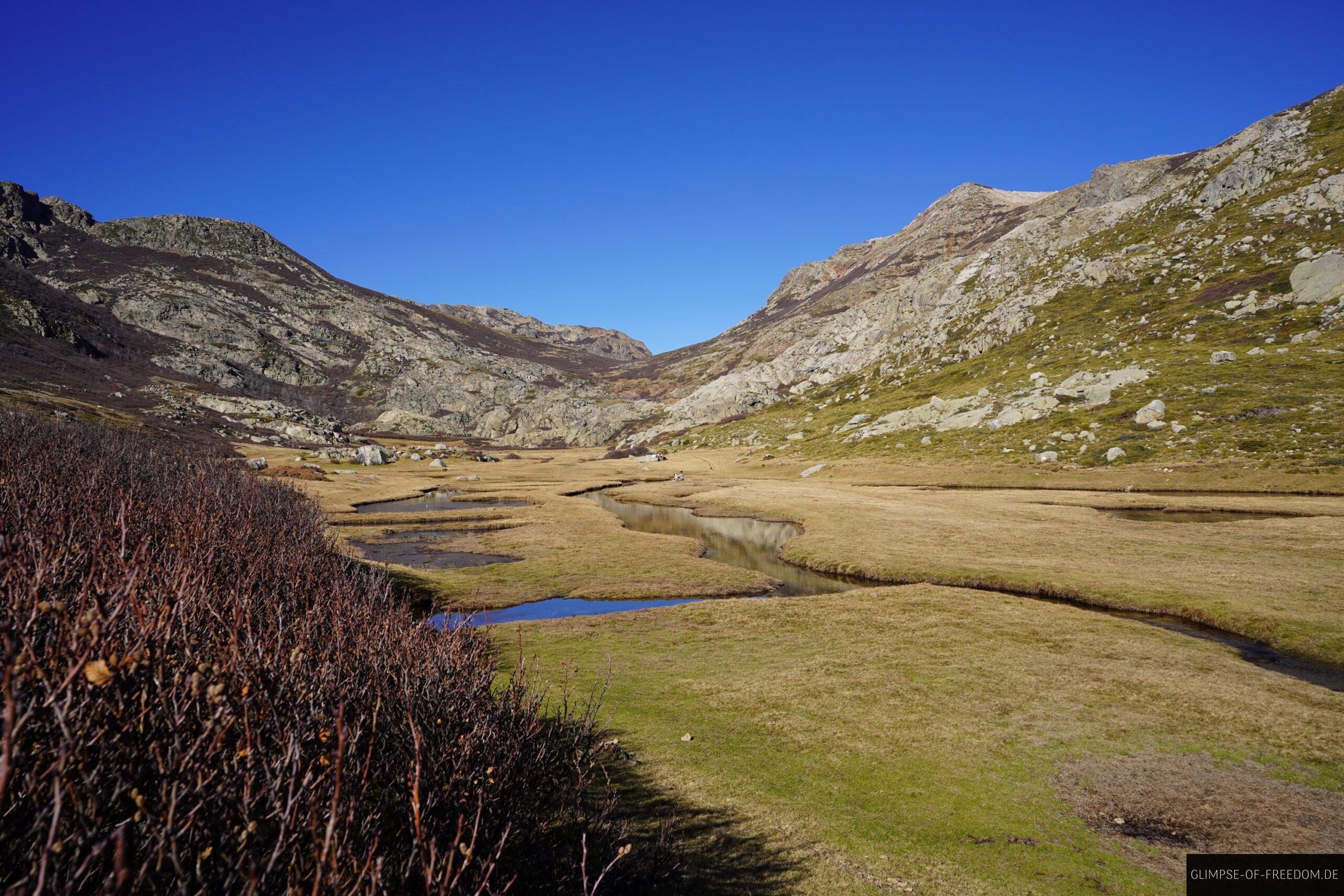 korsika pozzi seen moorlandschaft wanderung scaled Korsika Pozzi Seen Wanderung: Moorlandschaft mit Bach und Bergen unter blauem Himmel.